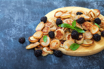 Minipancakes, blackberries and mint leaves on a black wooden background. Dessert. Copy spaes.