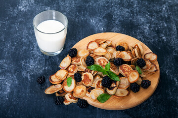 Minipancakes and blackberries, a glass of milk on a black background. Dessert. Copy spaes.