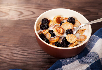 Delicious and healthy dessert of minipuncakes and blackberries with milk in a ceramic cup on a wooden table. Copy spaes.