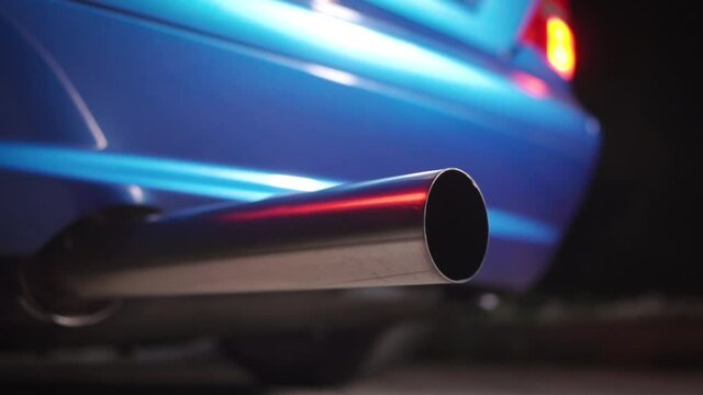 Close up of the exhaust pipe of a tuned sports car. Footage. Part symbol and conceptual tuning, motorsport, workshops, background. Vehicle standing on an asphalt road on a clear weather.