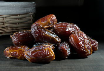 Macro photography, or close up of a group of dates on a wooden table with a handmade basket in the background in a dark environment