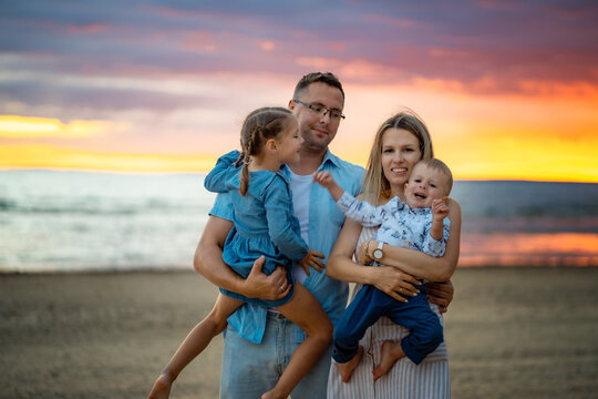 portrait of happy caucasian family. Mother holding a little son in arms. father holding a cute smiling daughter. Summer sunset at the beach. Image with selective focus. 