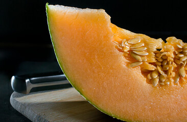 close up or macro photography of melon with seeds on a cutting board with rim light and in a black...