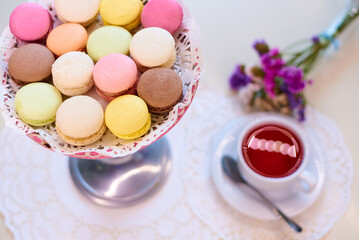 Fototapeta na wymiar Coloured macaroons with red tea on a table with flowers.
