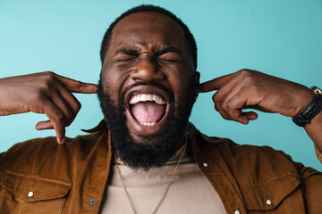 Displeased african american man screaming and plugging his ears