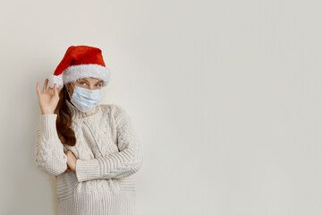 Young beautiful woman wearing mask and santa hat standing over isolated beige background looking side confident, thinking with crossed arms