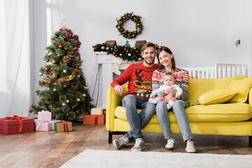 Obraz na płótnie Canvas happy family with baby boy sitting on sofa near christmas tree