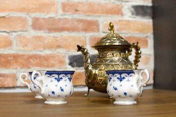 A modern teapot for tea and a cup on the kitchen table on the brick wall hair dryer. Tea set