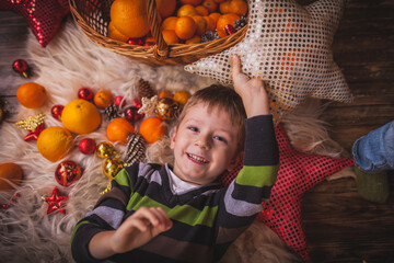 Fototapeta na wymiar Christmas boy lying on his skin around tangerine toys ornaments for Christmas tree