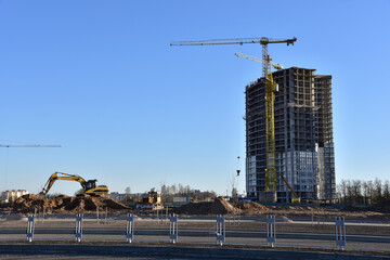 View on the large construction site with tower cranes and buildings. Excavator on Road work and earthworks for infrastructure improvement. Sewerage and communications laying.