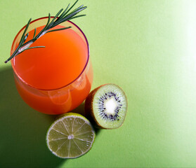 Composition of glasses with orange juice, lime, kiwi and verdure on a light green background