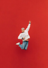 Guy is levitating on a background of a red wall with a laptop in his hands. Photo of a young male student in a jump on a red background. Vertical.