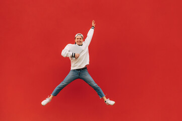 Fototapeta na wymiar Happy guy in stylish casual clothes jumps on a background of a red wall with a smile on his face and a laptop in his hands. Background. Isolated.