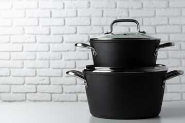 Black kitchenware on table against white brick wall