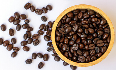 top view of dark brown roasted organic coffee bean in a wooden on white background. Selective focus on coffee beans in a bowl