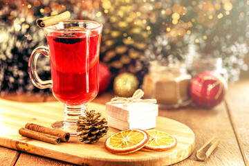 Mulled red wine with spices and Christmas fruits on a rustic wooden table with Christmas colors and lights. Traditional hot drink at Christmas time