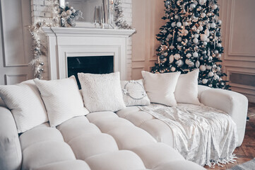 Decorated Christmas tree and cozy sofa in white classic New Year's living room holiday interior