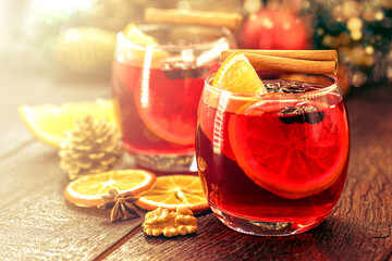 Mulled red wine with spices and Christmas fruits on a rustic wooden table with Christmas colors and lights. Traditional hot drink at Christmas time