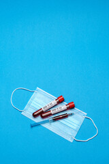 Syringe, test tube with blood sample and disposable face mask to prevent COVID-19 virus on blue background