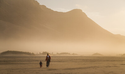 Silhouette of a young mother walking with her little child on a summer day in Cofete, Fuerteventura, Canary Islands, Spain.