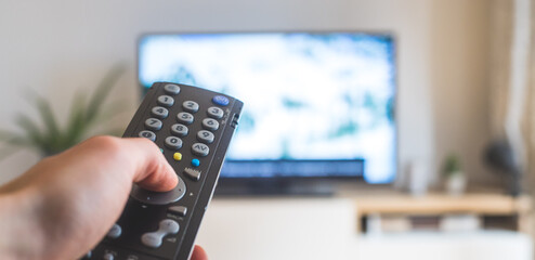 Male hand is holding TV remote control, streaming on a smart TV.