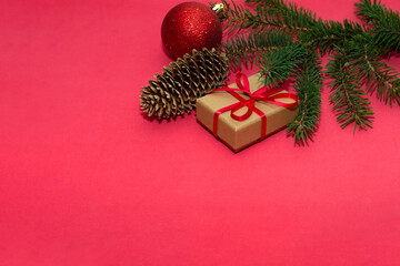 Natural spruce tree branch with a fir cone and Christmas decorations on a red background. Merry christmas and New Year. A minimalist composition, celebration and giving gifts. Copy space, flat lay.