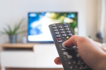 Male hand is holding TV remote control, streaming on a smart TV.