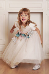 Fototapeta premium cute little blond baby girl with long hair in white dress smiling grimacing