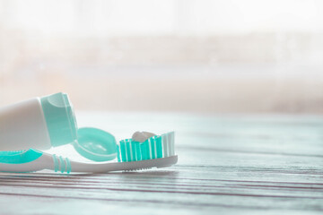 Turquoise toothbrush with white toothpaste on the bristles and a tube of toothpaste on a white...