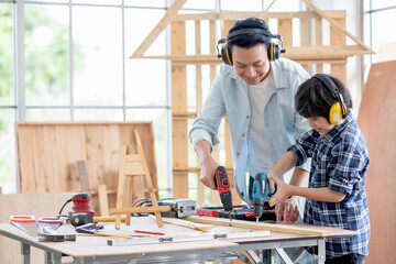 Asian father with noise canceling headphone teach and show to his son to use electric drill to work...