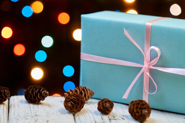 A blue Christmas or New Year gift box with pink ribbon on wooden surface against of colorful lights. Close-up, selective focus
