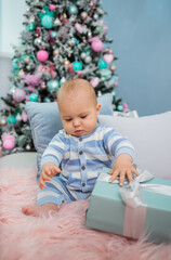 Fototapeta na wymiar baby boy in pajamas sitting on a fur blanket with pillows and gifts on the background of a Christmas tree