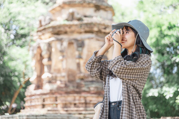 Beautiful young asian female traveler taking a photo with retro camera while traveling in popular tourist attraction thailand ancient temple.