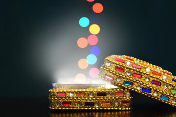 A colorful jeweled box with open lid and white light shining from within. Colorful balls of light appear to rise from out of the box. Dark background.