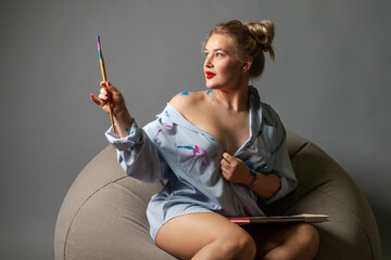 girl artist with brushes in a shirt stained with paints.