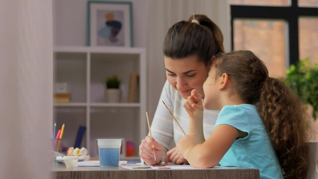 family, motherhood and leisure concept - mother spending time with her little daughter drawing with colors and gossiping at home