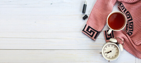 A cup of hot tea, knitted sweater, alarm clock and perfume on wooden light table. banner. winter morning concept