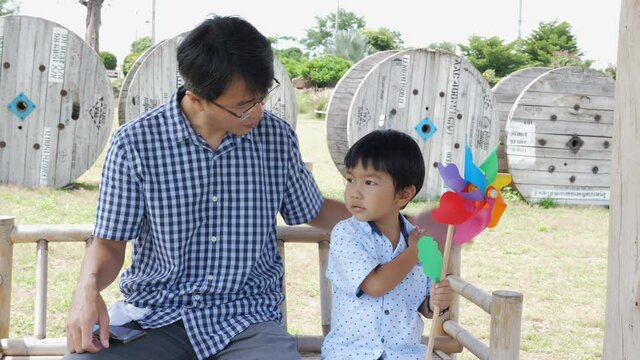4K Asian cute child boy and father travel together outdoor. Kid hold turbine toy blowing by wind. Happy family travel and wind energy power concept.