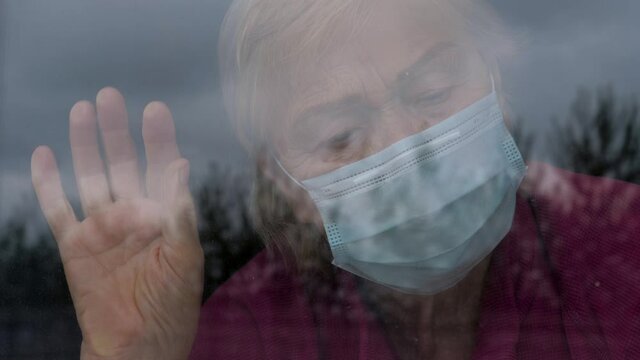Woman In Medical Mask Looks Sadly Out Of Window At Street Because Of Covis-19
