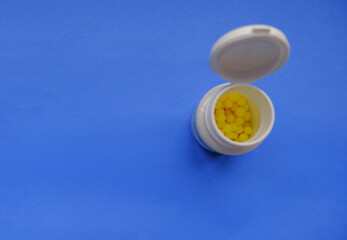 Yellow pills in white plastic container close-up on blue background. Copy space. Top view. Medicine, healthcare, prevention