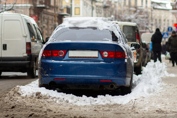 Cars parked on a side of city street covered with dirty snow in winter.