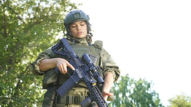 Portrait of confident military woman with a gun in forest, hunter female in camouflage suit with a gun stand in nature alone.