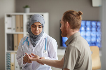 Fototapeta na wymiar Nurse in hijab examining the pulse of patient during medical exam while he visiting the doctor's office