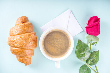 Valentine Day Morning background. Valentine Breakfast with Cup of Coffee, fresh Croissants and red Roses Flowers on turquoise background.