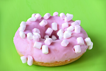 Strawberry donut covered with pink icing on green background.