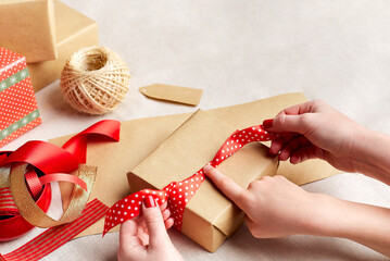 Mother and child hands wrapping christmas gifts into brown paper and tying them up with red bows