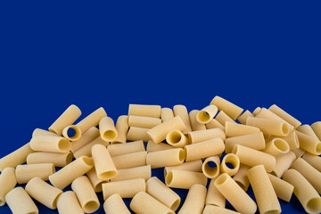 Paccheri macaroni Italian dry raw pasta bronze drawn, rough paste from Gragnano,Naples,Italy on blue background top view. Copy space