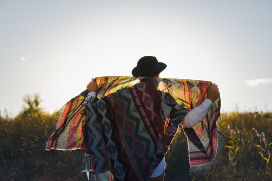 Man standing in a field poses with vintage poncho against the sun