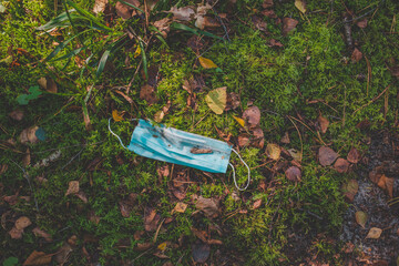 Medical face mask trash on the ground in forest. Environment pollution problem due to coronavirus pandemic.