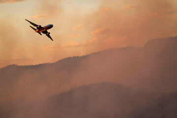 Military aircraft flying over smoke emitting from wildfire in forest during sunset